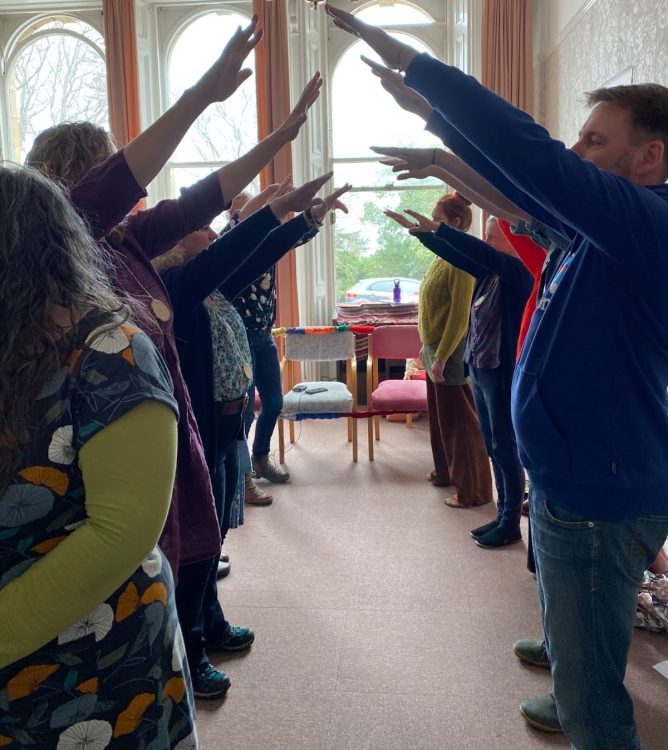 A photo of a group of people standing opposite each other towards each other with both arms outstretched towards the opposite person, some sort of ritual to welcome the new to be certified trainers. 